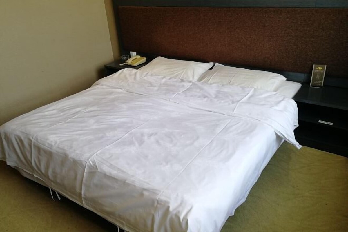 Ein ordentlich bezogenes Bett mit weißen Leinen, ein Nachttisch mit einer Lampe und ein weiterer Nachttisch mit einem Telefon.