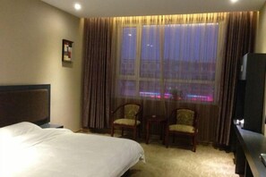 Ein Hotelzimmer mit einem Bett, zwei Stühlen, einem kleinen Tisch, einem Fernseher und einem Fenster mit Vorhängen.