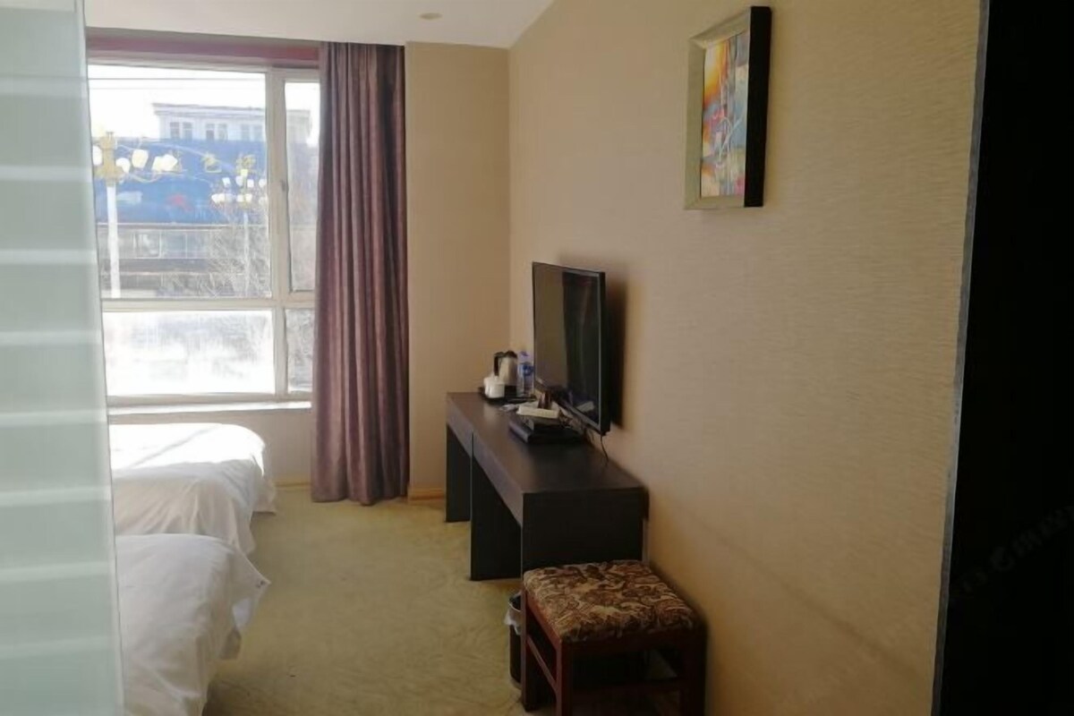 Ein Hotelzimmer mit zwei Betten, einem Fernseher auf einem Schrank, einem kleinen Tisch und einem Fenster mit Vorhängen.