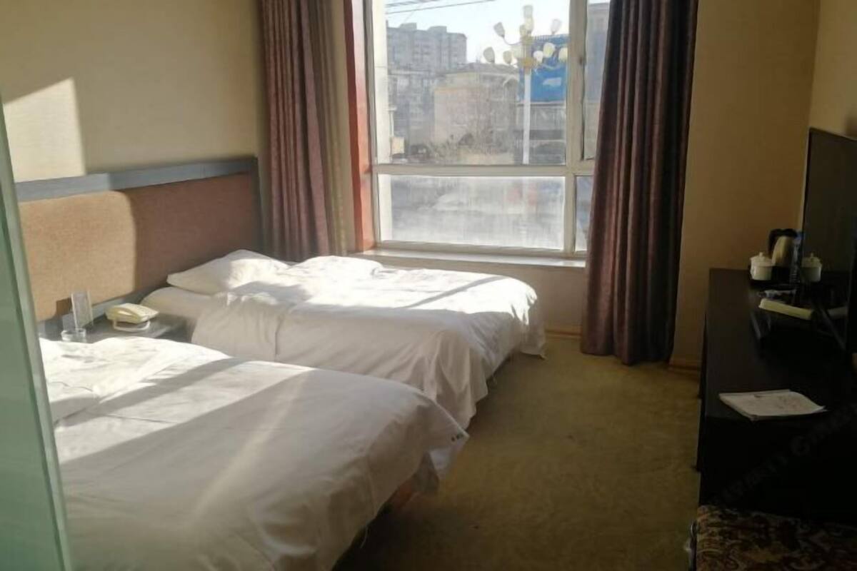 Une chambre d’hôtel avec deux lits, un bureau avec un téléphone, une télévision et une fenêtre avec des rideaux.