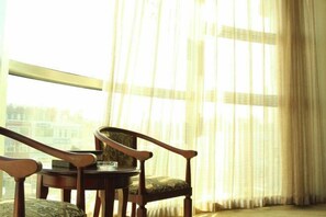 Ein Zimmer mit großem Fenster, einem runden Tisch und zwei Holzsesseln.