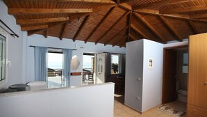Quarto com teto de madeira, pequeno kitchenette, vista exterior e banheiro com vaso sanitário e armário.