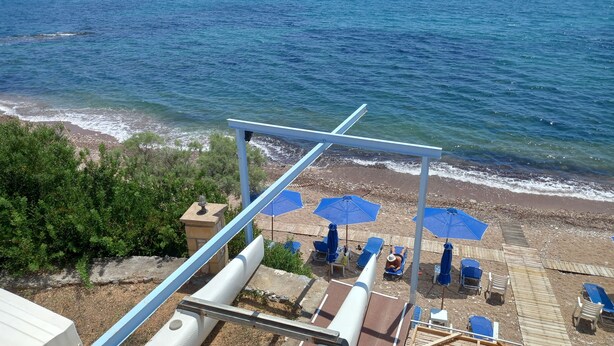 Uma praia com guarda-sóis azuis e espreguiçadeiras, um deck de madeira e vista para o mar.