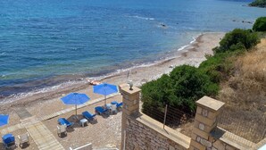 Uma praia com um muro de pedra, um deck de madeira e guarda-sóis azuis.