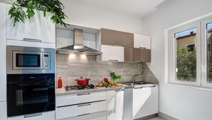 A modern kitchen with white cabinetry, a built-in microwave, a stove, and a large window providing a view of the outdoors.