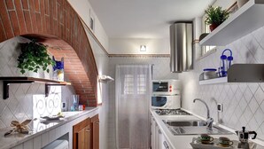 Une cuisine compacte avec une arche en briques, un dosseret de carreaux blancs, des appareils en acier inoxydable et une petite fenêtre.