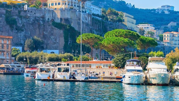 Un port de plaisance avec des bateaux amarrés, une falaise bordée de bâtiments et un ciel dégagé.