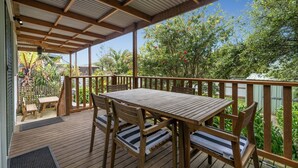 Una terraza de madera con una mesa y sillas, rodeada por un cerco de madera y abundante vegetación.