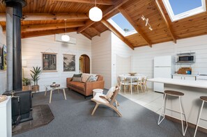 A spacious loft with a high ceiling, wooden beams, a fireplace, a dining area, and a kitchen. - The Beach Cottage (Separation Creek)