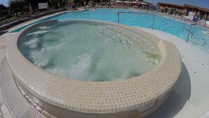 Tinaco con borde de azulejos, rodeado por un área de piscina con sillones y sombrillas.