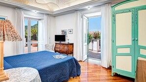 Een slaapkamer met een bed, een televisie, een bureau en een deur naar een balkon.