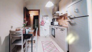 A compact kitchen with a refrigerator, stove, and microwave. There is a dining table with chairs and a vase with flowers. A door leads to another room.