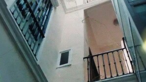 A view from a window overlooking a building's interior, including a balcony with a railing, a small window, and a door.