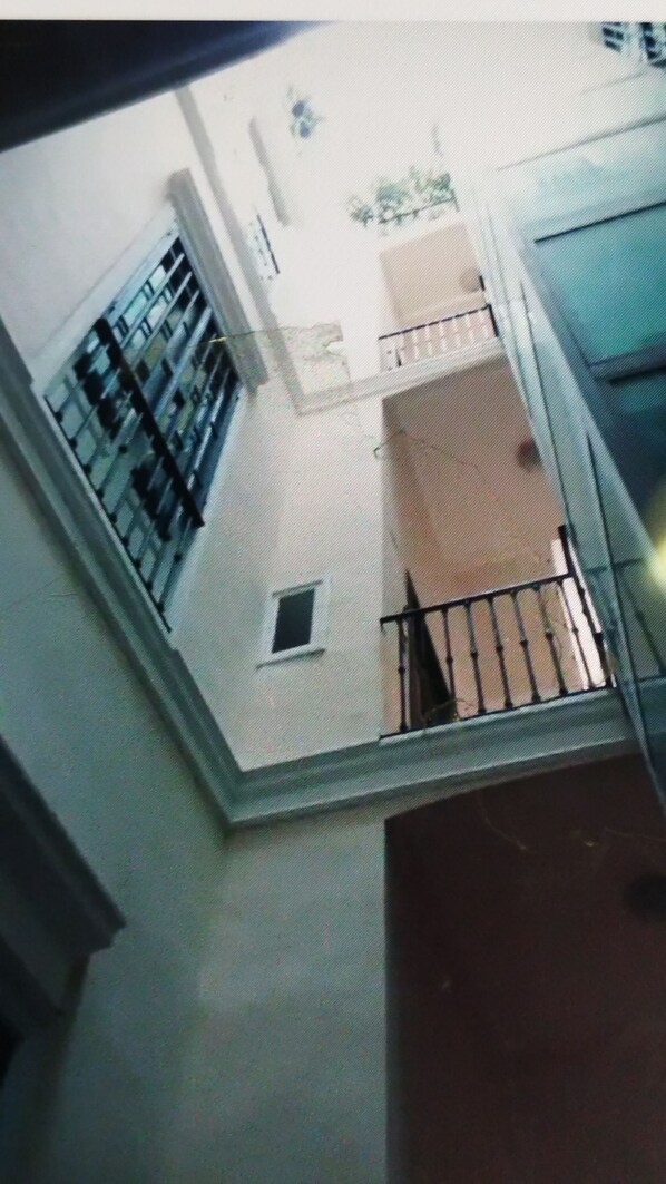 A view from a window overlooking a building's interior, including a balcony with a railing, a small window, and a door.