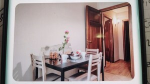 A dining area with a table set for two, a vase with flowers, and a door leading to another room.