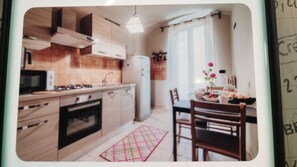 A kitchen with wooden cabinets, a microwave, a stove, and a refrigerator. There is a dining table with chairs and a vase of flowers. - Home flores (Bari)