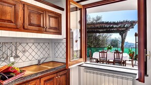 A kitchen with wooden cabinets, a tiled backsplash, and a large window opening to an outdoor dining area.