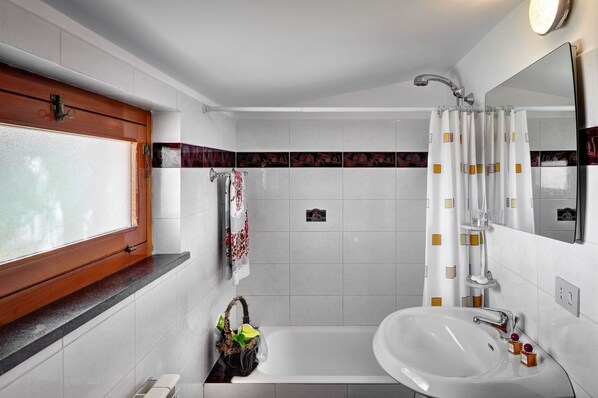 Ein Badezimmer mit einer Badewanne, einem Waschbecken, einem Spiegel und einem Fenster mit Holzrahmen.