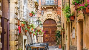 Un estrecho callejón con una puerta de madera, paredes de piedra y macetas colgantes.