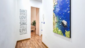 Un pasillo con una cita inspiradora en la pared, suelo de madera y un cuadro grande de una escena costera.