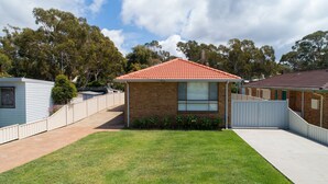 A single-story brick house with a red tiled roof, a fenced yard, and a clear blue sky. - Alka Beach House –  close to the beach (Callala Beach)