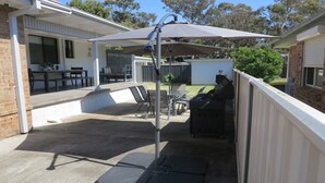 A covered patio area with a barbecue grill, outdoor seating, and a pergola providing shade. - Alka Beach House –  close to the beach (Callala Beach)
