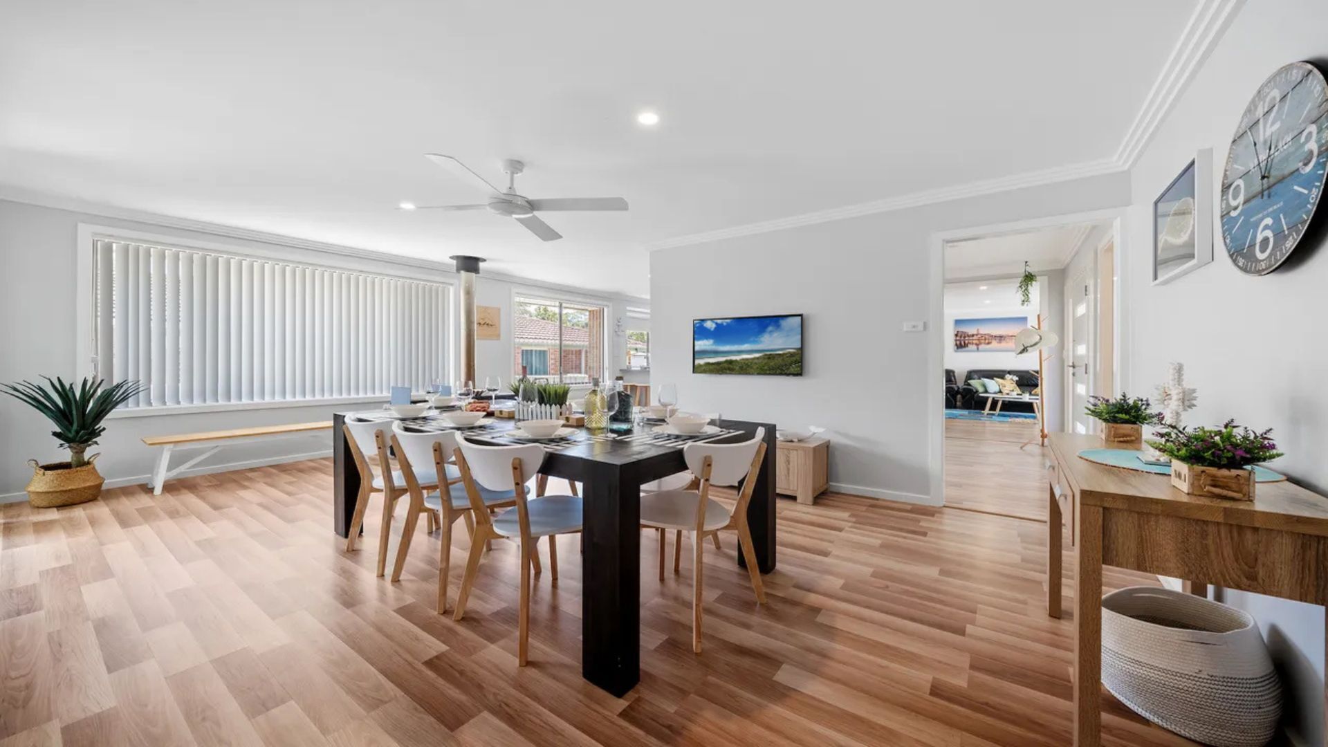 A spacious dining area with a black table, white chairs, and a ceiling fan.