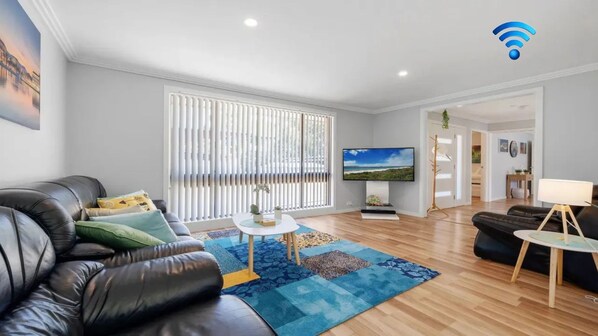A modern living room with a leather sofa, a flat-screen TV, and a blue patterned rug.