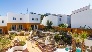 A modern hotel with white and orange exterior walls, a landscaped courtyard with palm trees, and a pool area. - 9 Balinese-style Houses with 3 Bedrooms, Communal Pool, and Jacuzzi (Roses)