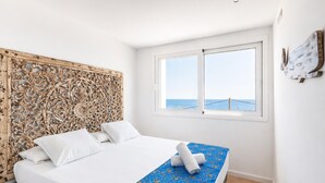 A bedroom with a bed, a window with a view of the sea, and a decorative headboard.