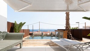 A rooftop pool area with a bench, lounge chairs, and a view of the sea.