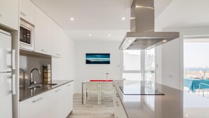 A modern kitchen with white cabinets, stainless steel appliances, and a dining area with a red tablecloth. - 3-bedroom apartment with sea views, communal jacuzzi, next to the beach and close to the town center (Roses)