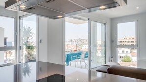 A modern kitchen with a large island, a stainless steel range hood, and a view of the city through large windows. - 3-bedroom apartment with sea views, communal jacuzzi, next to the beach and close to the town center (Roses)