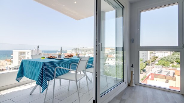 A balcony with a table set for dining, overlooking a cityscape and the sea. - 3-bedroom apartment with sea views, communal jacuzzi, next to the beach and close to the town center (Roses)