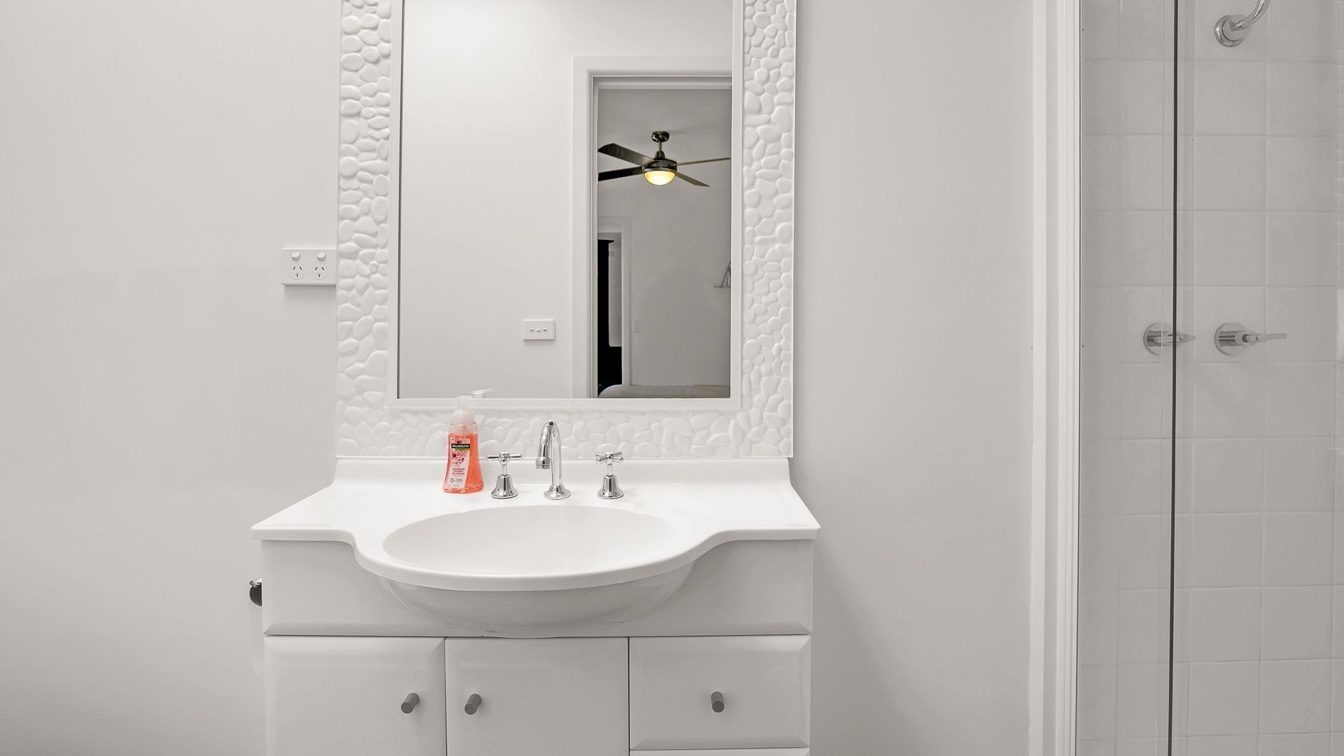 A bathroom with a white sink, a mirror, and a ceiling fan.