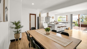 A modern kitchen with a central island, a dining area with a wooden table and chairs, and a large window providing a view of the outdoors.