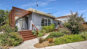 A modern house with a wooden deck, a covered porch, and a garden with various plants and flowers. - Encanto in central Cowes (Cowes)