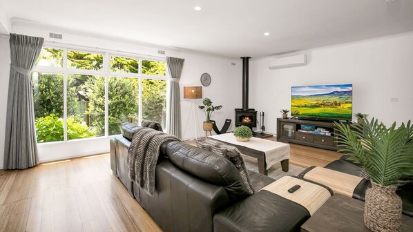 A modern living room with a leather sofa, a TV, a fireplace, and large windows overlooking a garden. - Encanto in central Cowes (Cowes)