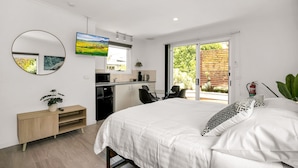A modern bedroom with a bed, a desk, and a kitchenette.