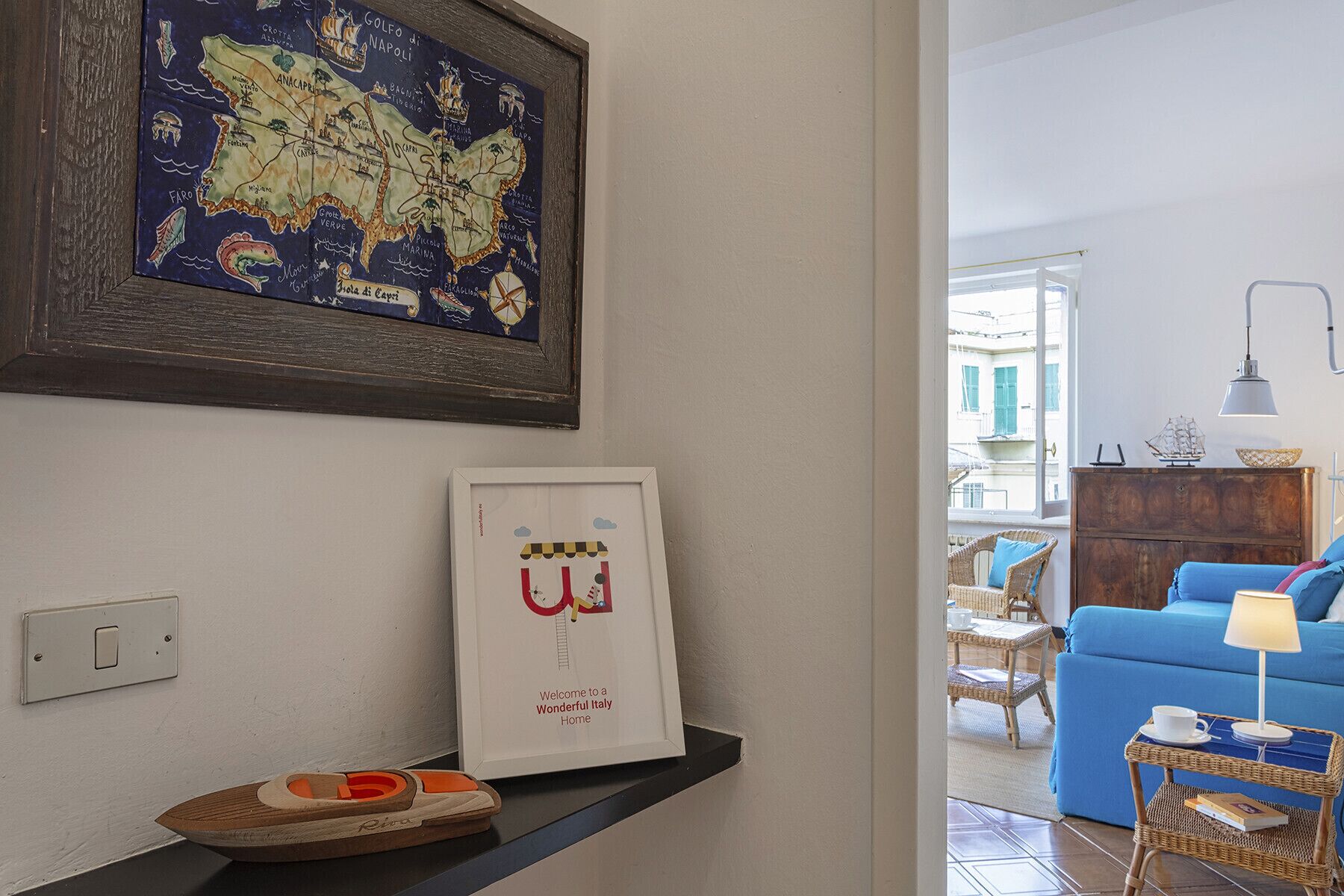 A living room with a framed map, a framed welcome sign, a wicker side table, and a blue sofa.