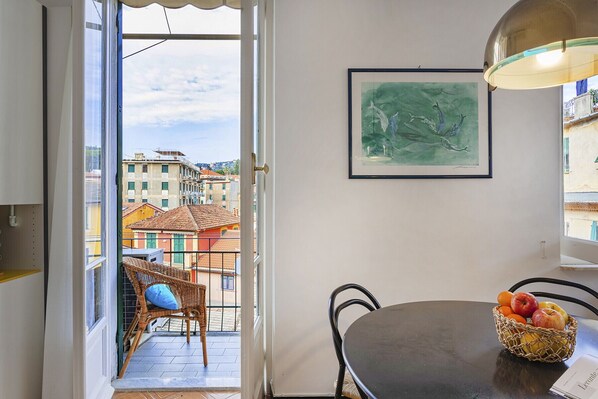 A balcony with wicker chairs, a table with a fruit basket, and a framed painting on the wall.
