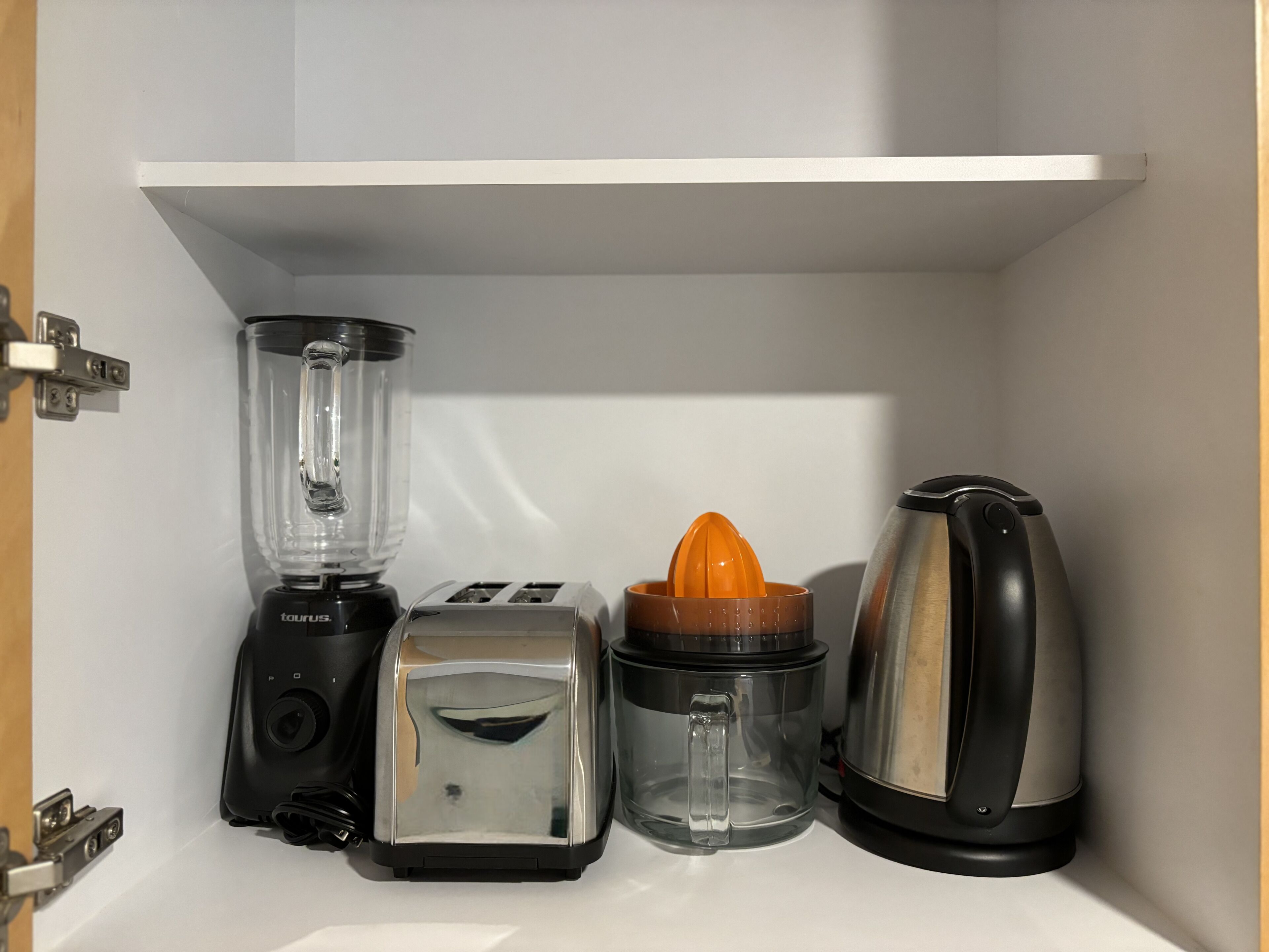 A kitchen with a blender, toaster, orange juicer, and kettle.