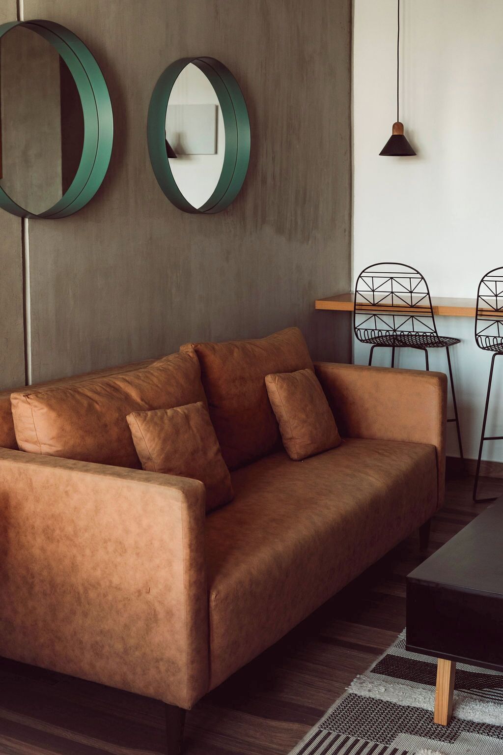 A modern living room with a brown leather sofa, two round mirrors, a wooden coffee table, and a geometric chair.