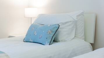 Una cama bien hecha con ropa blanca y una única almohada azul con estampado de concha.