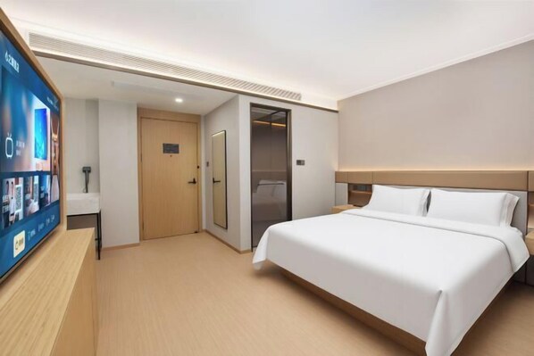 A hotel room with a bed, a television, a door, and a ceiling vent.