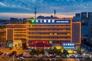 Un hôtel à plusieurs étages, une enseigne bien visible indiquant « Heart Edge Hotel », et un parking où sont garées plusieurs voitures.