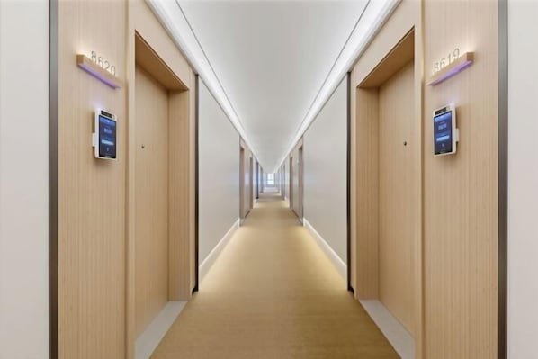 A hotel hallway with a carpeted floor, wooden walls, and illuminated room numbers.