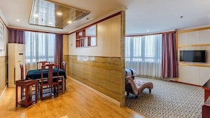 A hotel room with a wooden floor, a dining area with a table and chairs, a bed, a TV, and a patterned carpet. - Xinzhiyuan Yue Hotel (Hefei South Station Luogang Central Park) (Hefei)