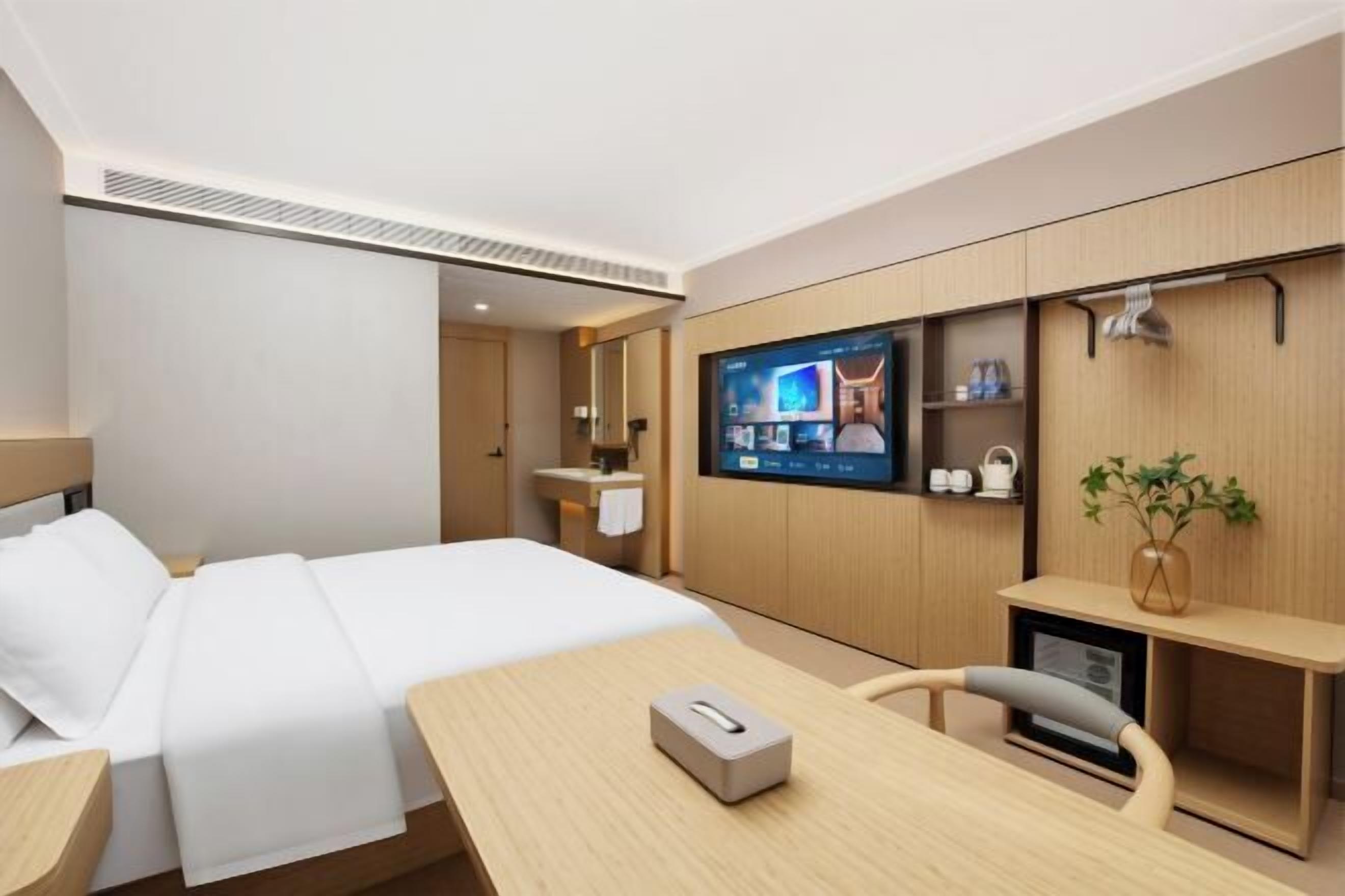 Une chambre d’hôtel moderne équipée d’un lit, d’une table de chevet, d’une télévision et d’un petit bureau.