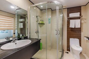 Moderni kylpyhuone, jossa on lasiseinällä varustettu suihku, valkoinen pesuallas ja wc-istuin.